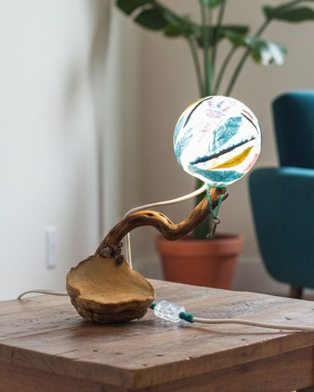 Lámpara de diseño orgánico con base de madera y esfera de luz en una sala de estar.